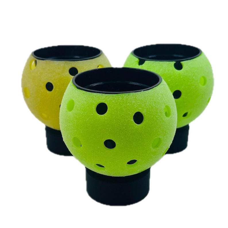 May include: Three spherical pickleball-style containers featuring a textured, perforated surface in shades of yellow and lime green. Each container has a wide, circular opening with a black interior rim and a solid black cylindrical base.