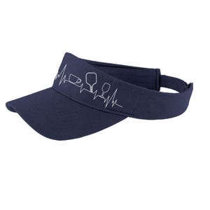 Op de afbeelding: Een marineblauwe visor met een witte omtrek van een hartslag, een koffiekopje, een peddel en een wijnglas.