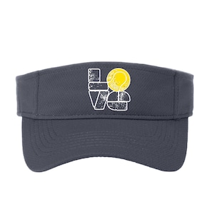 Puede incluir: Visera de tenis gris oscuro con la palabra "LOVE" en blanco, con una pelota de tenis amarilla en lugar de la "O". La visera está hecha de una tela transpirable y tiene una visera curva.
