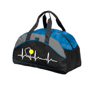 May include: A black and blue duffel bag featuring a grey accent panel and two black handles. The front displays a white heartbeat line graphic that incorporates a pickleball paddle silhouette and a bright yellow pickleball with holes.
