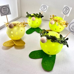 May include: Four yellow and green gnome-like figures with a wreath and a sign that says "veni vidi vici" on a white background.