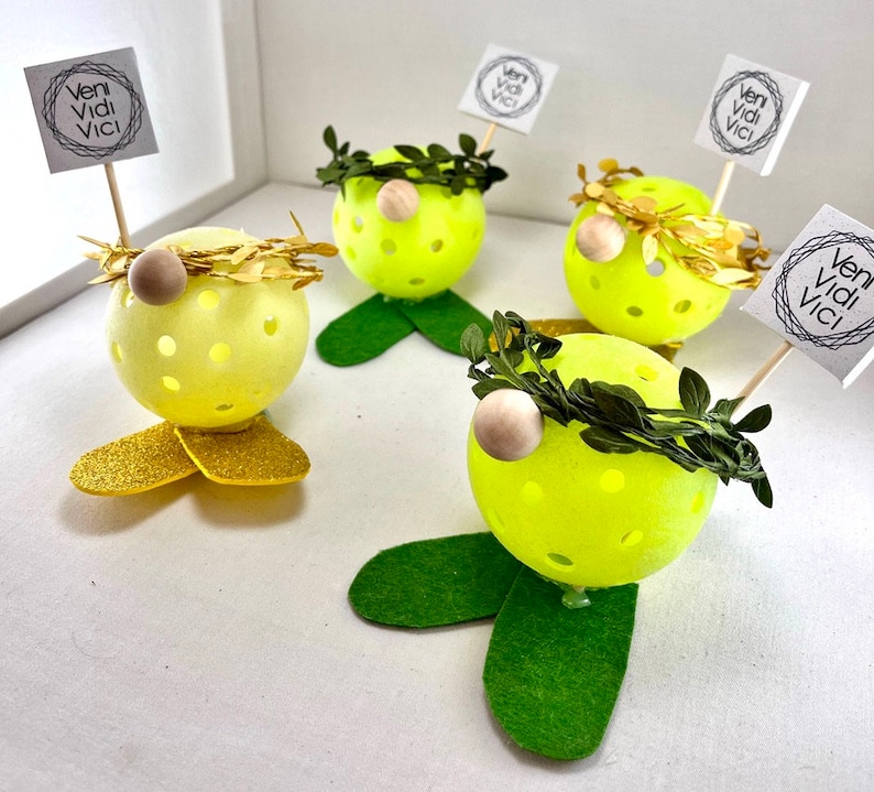 May include: Four yellow and green gnome-like figures with a wreath and a sign that says "veni vidi vici" on a white background.