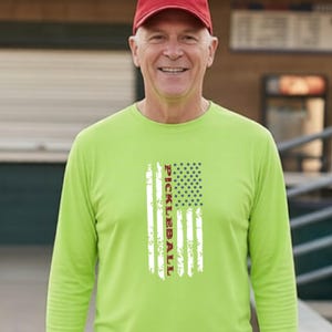 A lime green long-sleeve shirt featuring a vertical graphic of an American flag design with a distressed texture. The word PICKLEBALL is printed vertically in dark red capital letters within the center of the flag graphic.