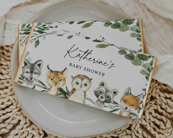 May include: A white and green baby shower favor box with a gold border. The box features a watercolor illustration of woodland animals, including a fox, raccoon, owl, lynx, and wolf. The text "Katherine's Baby Shower" is printed on the box.