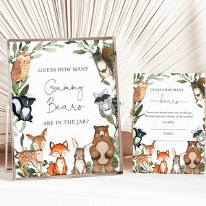 Puede incluir: Una tarjeta de juego imprimible para un baby shower con temática de bosque. La tarjeta presenta un oso marrón, un zorro, un ciervo, un conejo y un búho. El texto en la tarjeta dice "Adivina cuántos ositos de goma hay en el frasco?"