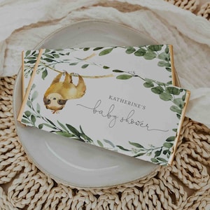 May include: A white card with green foliage and a sloth hanging from a branch. The card says "Katherine's Baby Shower" in cursive.