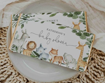 May include: A white chocolate bar wrapper with a jungle theme. The wrapper features a watercolor illustration of animals like a zebra, lion, rhino, tiger, elephant, and giraffe. The text on the wrapper reads "Katherine's baby shower".