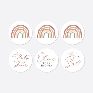 Op de afbeelding: Zes ronde stickers met een aquarel regenboogontwerp. Drie stickers hebben de tekst "Baby shower", "Olivia's Baby Shower" en "It's a Girl!" in een cursief lettertype.