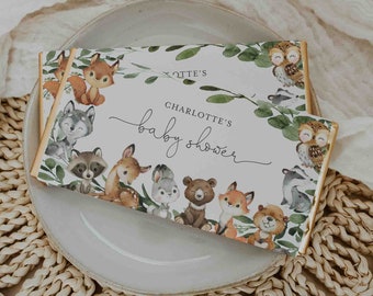 May include: A white chocolate bar wrapper with a woodland theme. The wrapper features a variety of woodland animals, including a fox, a raccoon, a deer, a bear, and an owl. The text on the wrapper reads "Charlotte's Baby Shower".