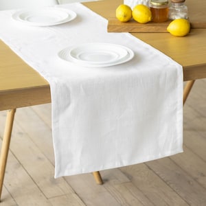 May include: White linen table runner on a wooden table with two white plates and lemons on a wooden chopping board.