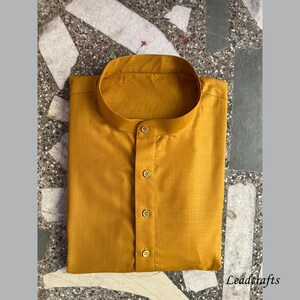 May include: A mustard yellow kurta with a mandarin collar and a button-up front. The kurta is made of a soft, lightweight fabric and has a subtle sheen.
