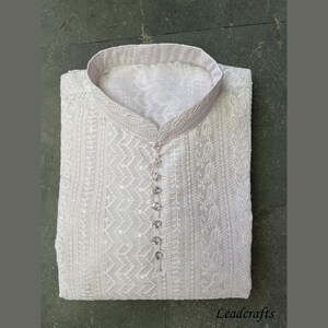 May include: A white embroidered kurta with a button-up closure. The kurta features a delicate floral and geometric pattern.