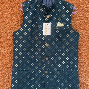 May include: A dark teal vest with a repeating pattern of small, reflective squares. The vest has a mandarin collar, a pocket, and gold-colored buttons. A tag with the text "LEADCRAFTS" is attached.