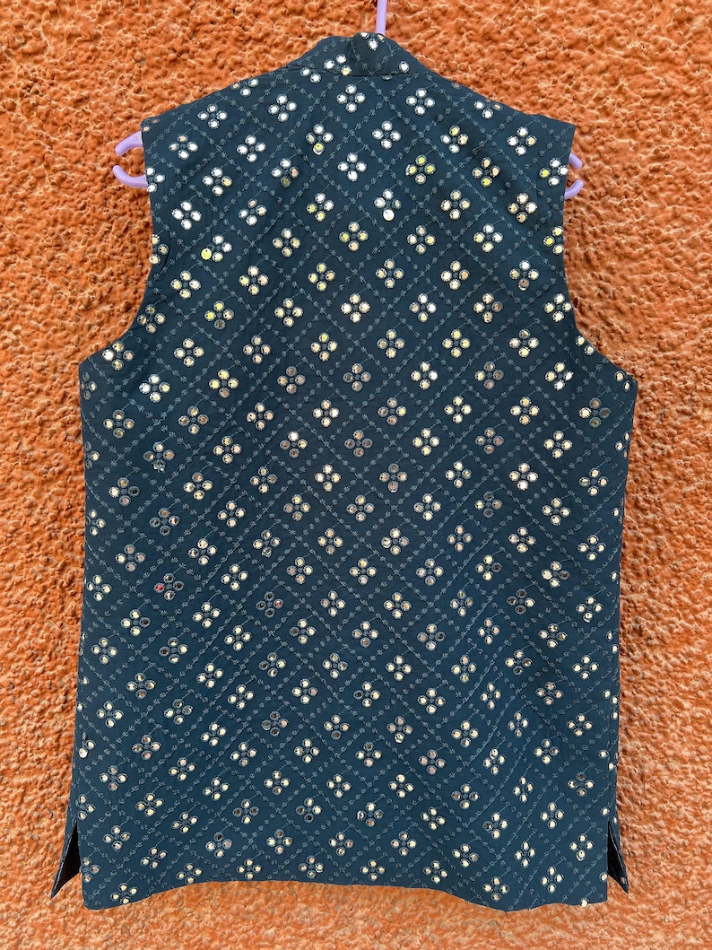 May include: A dark navy blue vest with a quilted pattern and small, reflective embellishments. The vest is sleeveless and has a mandarin collar. The embellishments are arranged in a repeating floral pattern across the vest's surface.