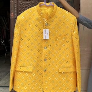 Puede incluir: Chaqueta amarilla brillante con un patrón acolchado y pequeños adornos reflectantes. La chaqueta tiene cuello mandarín, cierres de botón y dos bolsillos delanteros. Una etiqueta con el texto "PLEASURE CRAFTS" está adjunta.