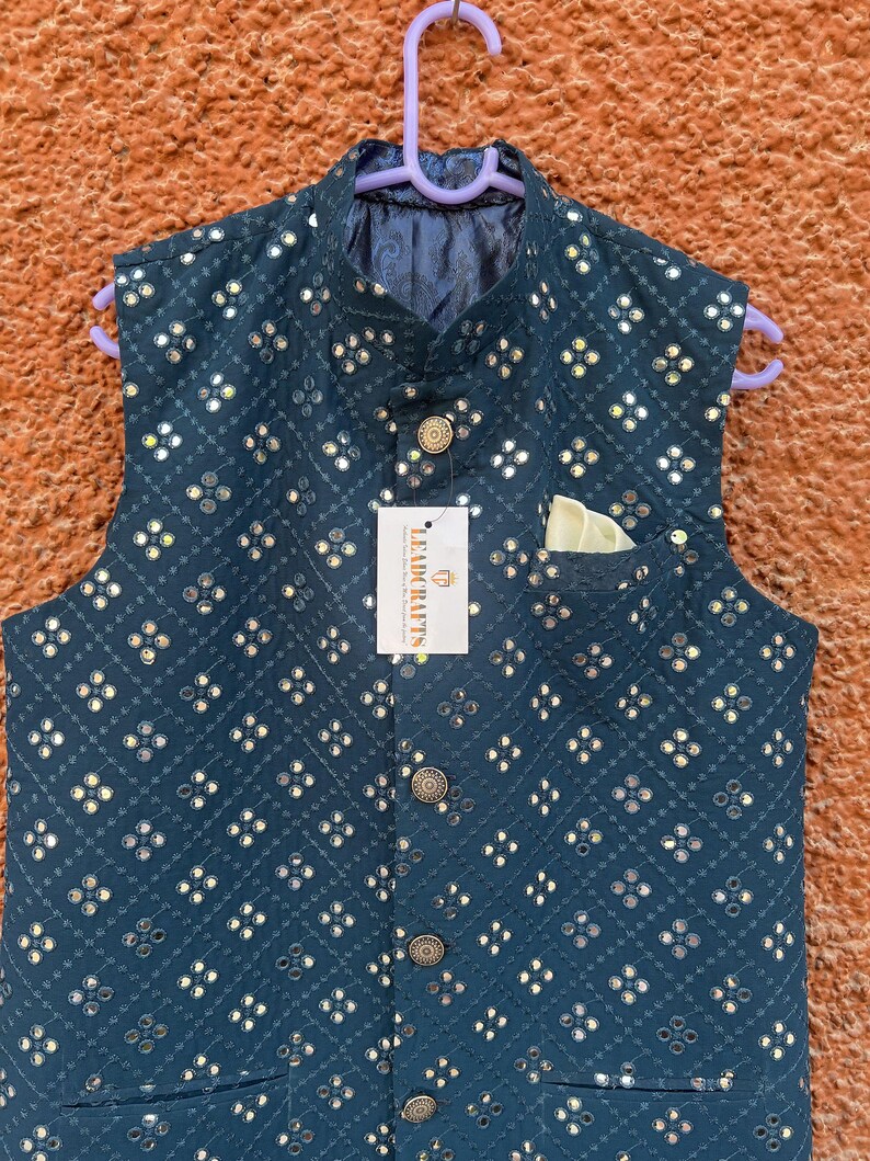May include: A teal-colored, sleeveless vest with a repeating pattern of small, reflective embellishments. The vest has a mandarin collar, a pocket square, and decorative buttons. A tag reads "LEADCRAFTS".
