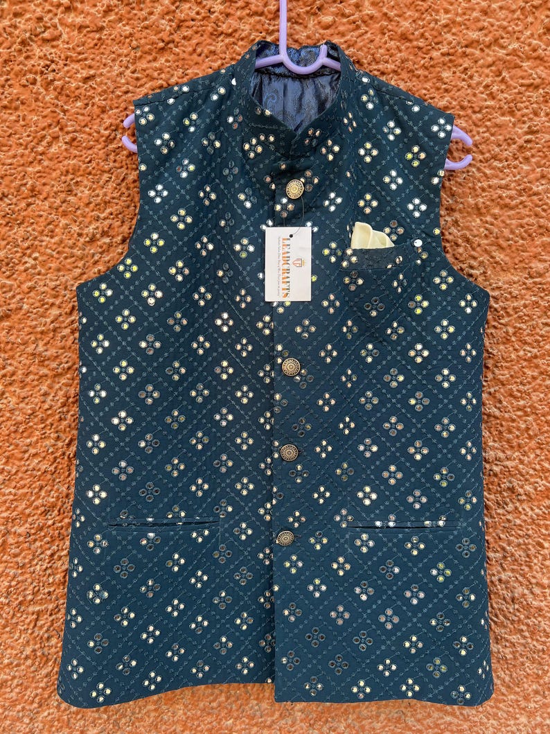 May include: A dark teal vest with a repeating pattern of small, reflective squares. The vest has a mandarin collar, a pocket square, and gold-colored buttons. A tag reads "LEADRAFTS". The vest is hanging on a purple hanger.