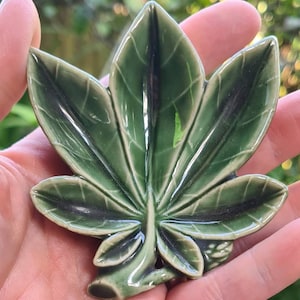 Könnte beinhalten: Eine Keramik-Blatt-Schale in grüner Glasur mit einem dunkelgrünen Adernmuster. Die Schale ist in Form eines Ahornblattes und hat ein kleines Loch in der Mitte.