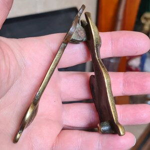 May include: A brass door knocker in the shape of a stylized animal. The knocker is hinged and has a detailed design.