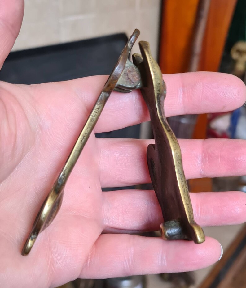 May include: A brass door knocker in the shape of a stylized animal. The knocker is hinged and has a detailed design.