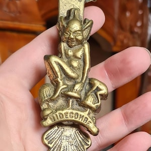 Peut inclure: Un heurtoir de porte en métal doré en forme de gobelin assis sur un champignon. Le heurtoir porte l'inscription "Widecombe".