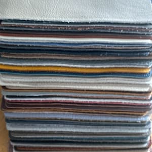 May include: A stack of different coloured leather swatches. The swatches are arranged in a neat pile, with the top swatch being a light grey colour.