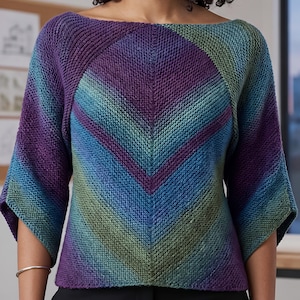 May include: A knitted top with a boat neck and three-quarter sleeves. The top features a chevron design in shades of purple, blue, and green. The sleeves are a solid blue-green color. The top is made of a soft, textured yarn.