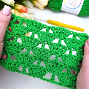 Può includere: Primo piano di un tessuto lavorato a uncinetto verde con un motivo ripetitivo di piccoli cerchi e spazi vuoti. Il tessuto è tenuto nelle mani di una persona.