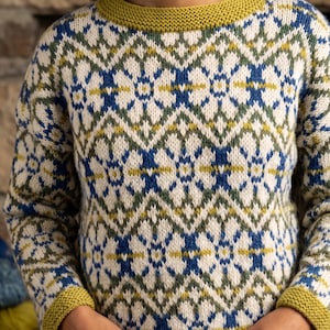 May include: A knitted sweater with a geometric pattern in cream, blue, green, and yellow. The sweater has a crew neck and ribbed cuffs and hem in a mustard yellow color. The design features a repeating diamond and floral motif.
