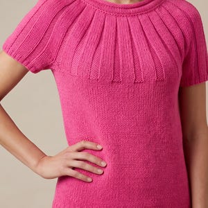 May include: A bright pink short-sleeved knit sweater featuring a ribbed crew neckline and vertical ribbed detailing extending from the collar across the shoulders and upper chest, with a smooth stockinette stitch body and a ribbed hem at the waist.