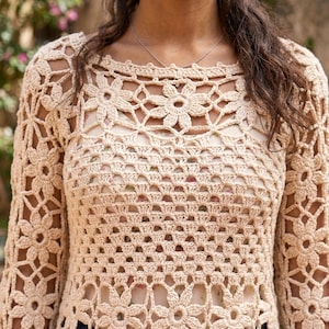 Puede incluir: Top de ganchillo beige con mangas largas y un patrón floral. El diseño calado revela una parte de la capa inferior. El top tiene un cuello redondo y está hecho de un hilo suave y de aspecto natural.
