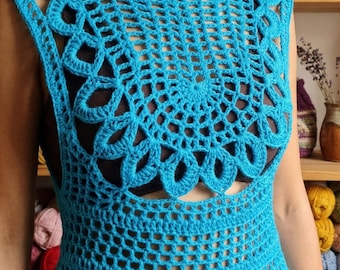 Pode incluir: Uma blusa sem mangas em crochê na cor turquesa brilhante, apresentando um padrão circular intrincado inspirado em mandalas no peito e ombros, transicionando para um design de grade aberta que se estende até uma bainha com acabamento festonado.