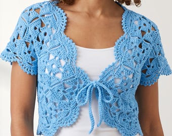 May include: A light blue crochet bolero featuring an intricate floral-inspired openwork pattern, short sleeves, and a front tie closure. The garment is worn over a plain white tank top, showcasing the detailed stitching and scalloped edges.
