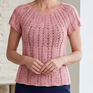Puede incluir: Una blusa de punto de manga corta en color rosa empolvado con cuello redondo y un patrón vertical de paneles alternos en punto liso y delicadas columnas de encaje calado que se extienden desde el cuello hasta el dobladillo.