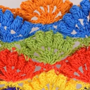 May include: A close-up of a multi-coloured crocheted doily with a rainbow pattern. The doily is made of yarn in shades of orange, yellow, green, blue, and red.