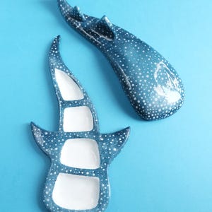 Puede incluir: Dos platos de cerámica con forma de tiburón ballena con un acabado azul brillante y patrones de lunares blancos. Un plato se muestra desde arriba, revelando tres compartimentos interiores blancos, mientras que el otro se muestra desde atrás, exhibiendo el exterior azul moteado.