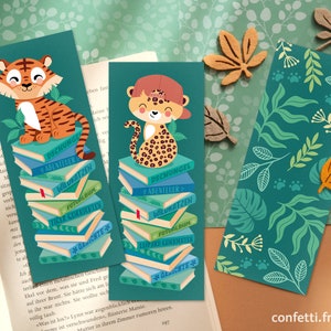 Puede incluir: Tres marcapáginas coloridos con animales de la jungla y pilas de libros. Los marcapáginas son verdes con un patrón de hojas de la jungla, un tigre con rayas naranjas y negras y un leopardo con manchas marrones y negras. El texto en los marcapáginas dice "Dschungel", "Abenteuer", "Wildkatzen", "Fotoalbum", "Tiger Geschichten", "Gepard Geschichten" y "Geschichten".