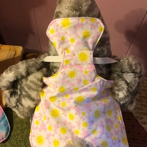 Peut inclure: Une selle de poulet, conçue pour protéger le dos d'une poule des blessures dues à l'accouplement du coq. La selle est blanche avec un motif floral rose et des centres jaunes. Une sangle élastique fixe la selle.