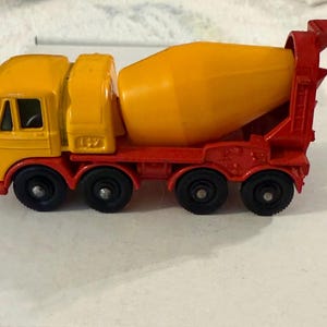May include: A toy cement mixer truck in yellow and red. The cab and mixer drum are yellow, while the chassis and support structure are red. The truck has four black wheels and is a classic toy vehicle.