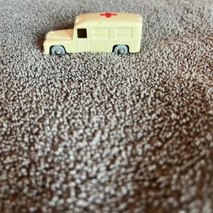 Può includere: Un'ambulanza giocattolo bianca con una croce rossa sul tetto. L'ambulanza ha ruote nere e la parola "AMBULANCE" stampata sul lato.