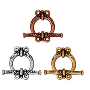 Puede incluir: Tres cierres de palanca ornamentados en tonos cobre, plata y oro. Cada cierre presenta un anillo decorativo y una barra con detalles intrincados, adecuados para la fabricación de joyas o proyectos de artesanía. Los cierres se muestran sobre un fondo blanco.