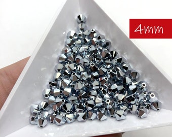 Puede incluir: Un montón de cuentas de cristal plateadas de 4 mm en una bandeja triangular blanca. 4 mm.