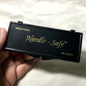 May include: A black, rectangular, magnetic needle storage case with the words "Needle-Safe" and "PATENTED" in gold lettering.