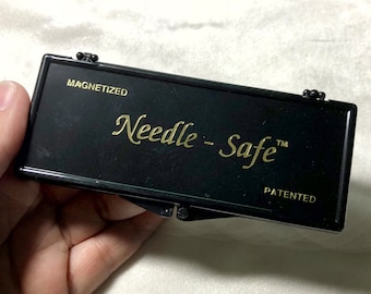 May include: A black, rectangular, magnetic needle storage case with the words "Needle-Safe" and "PATENTED" in gold lettering.