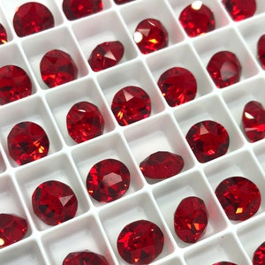 May include: A close-up view of a white tray filled with red, round, faceted rhinestones. The rhinestones are arranged in rows and columns.