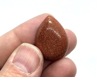 May include: A teardrop-shaped pendant made of red sandstone with a hole drilled at the top for stringing.