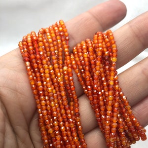 May include: Multiple strands of small, faceted, round orange beads strung on thin red thread. The beads have a translucent quality and a reflective surface, creating a bright, warm appearance across the collection of individual circular components.