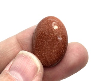 Puede incluir: Un cabujón de arenisca de color marrón rojizo liso, de forma ovalada, con una textura brillante y brillante.