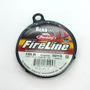 May include: A spool of Berkley FireLine microfused braided bead thread in a black container with a red and yellow label. The label reads "10LB Crystal 50YD 0.008in avg. dia FLBT10-CY 1389517".