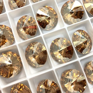 May include: A close-up view of a tray of round, faceted, amber-colored glass rhinestones. The rhinestones are arranged in a grid pattern and have a shiny, reflective surface.